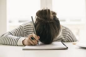 Woman, head down on blank notebook, holding pen--writer's block